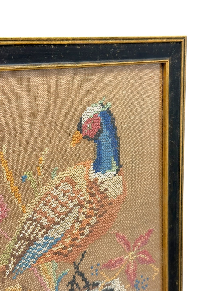 Close-up of vintage cross stitch art depicting bird in black and gold frame.