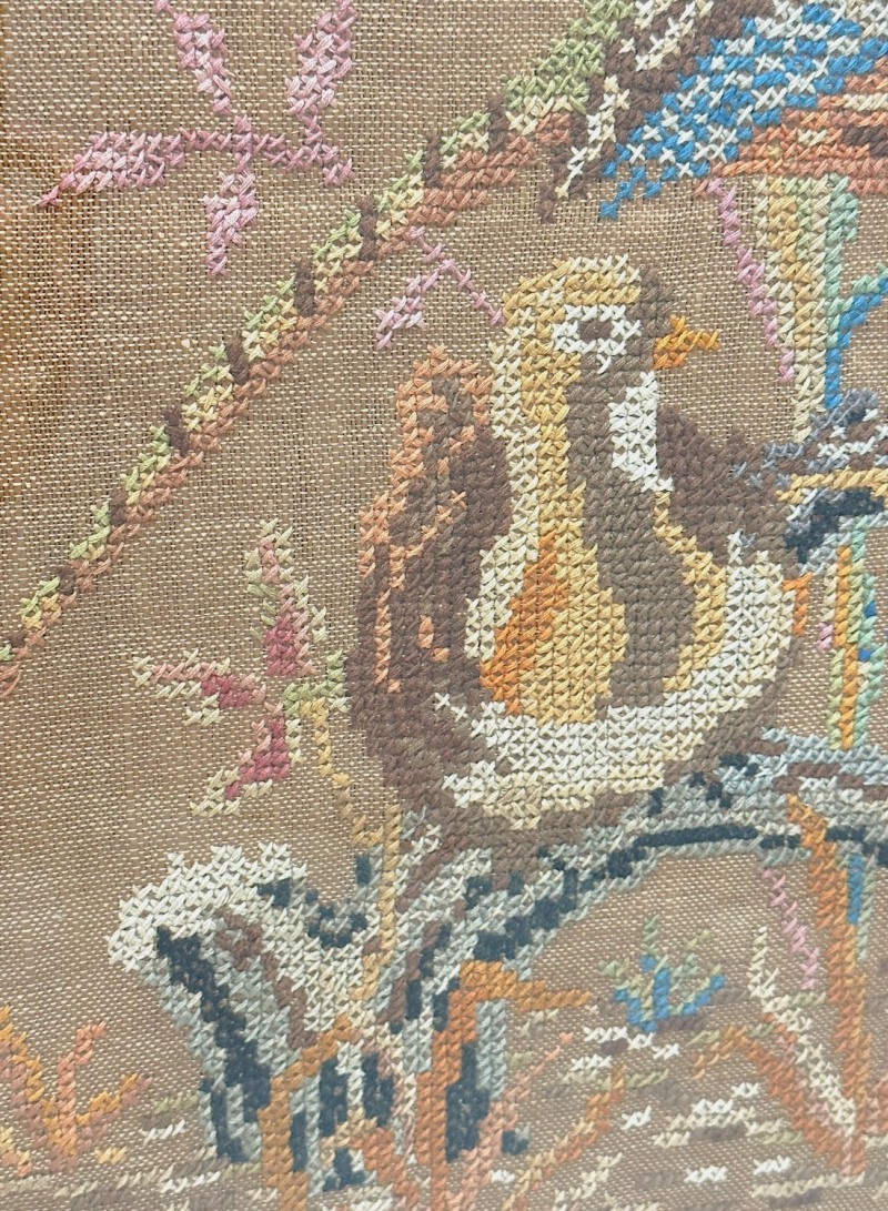 Close-up of vintage cross stitch bird art in black and gold frame.